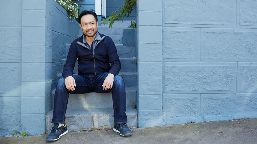 Person in navy zip-up sweater and jeans sitting on concrete steps against light blue painted wall