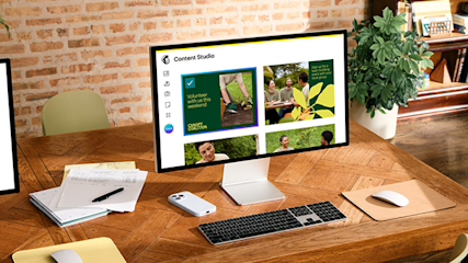 Computer monitor displaying Content Studio interface on wooden desk with keyboard, mouse, notebooks and office plants