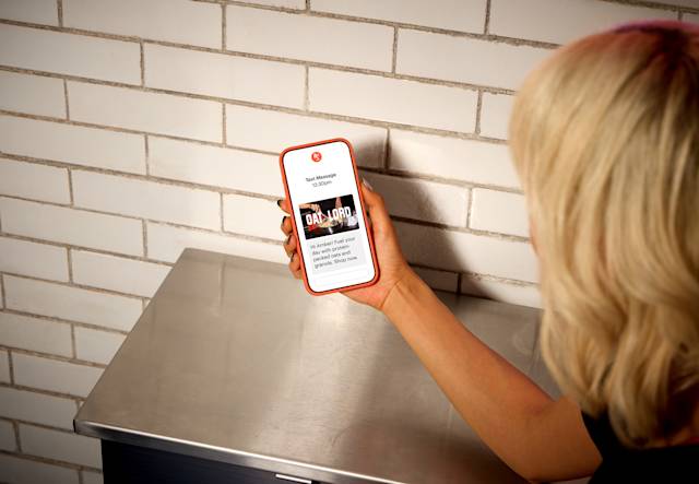 Person holding red iPhone displaying a promotional text message from Oat Lord about protein-packed oats and granola