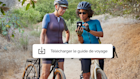 Deux femmes faisant une promenade à vélo, marquant une pause pour télécharger une application de guide de voyage offerte par une campagne Mailchimp.