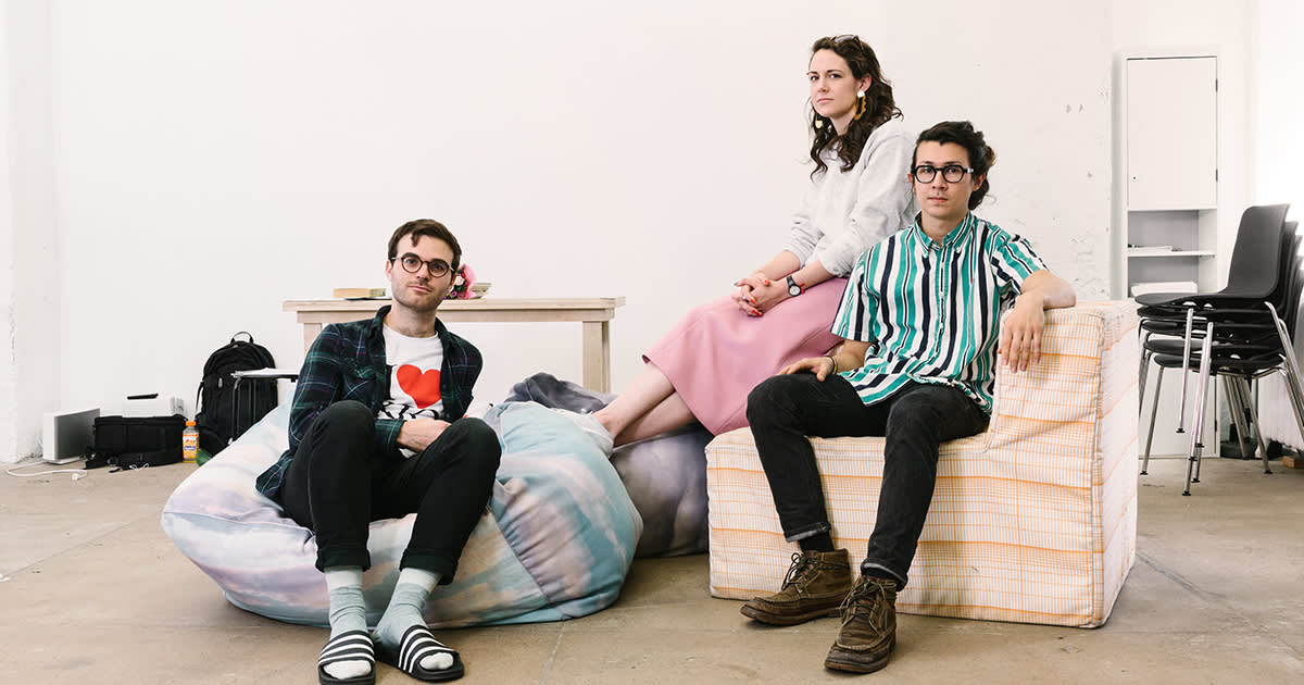 Three young professionals relaxing in a minimalist office space with bean bag and casual seating against white walls