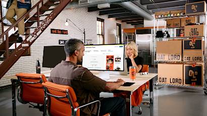 Team members working at modern office desks with orange chairs, surrounded by industrial-style decor and Goat Lord branding