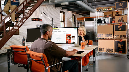 Team members working at modern office desks with orange chairs, surrounded by industrial-style decor and Goat Lord branding