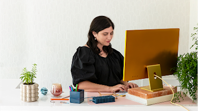 Professional working at modern desk with laptop, plants, and orange privacy screen in bright home office setting
