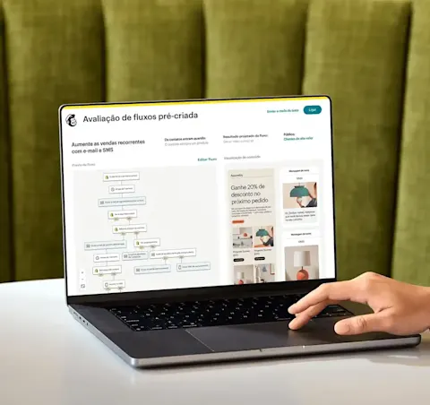 Imagem de uma pessoa sentada à mesa, olhando para a tela de um notebook que exibe o recurso de análise de modelo de fluxo do Mailchimp. O recurso mostra uma prévia de um fluxo de automação e uma visão abstrata das interfaces de e-mail e SMS da marca fictícia Assembly.