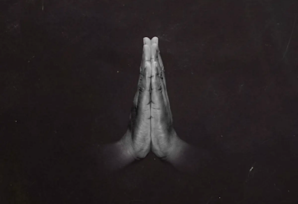 Hands pressed together in prayer position against dark background, shown in black and white monochrome