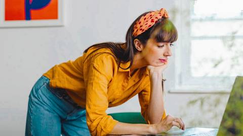 Woman wearing orange shirt and headband working on laptop