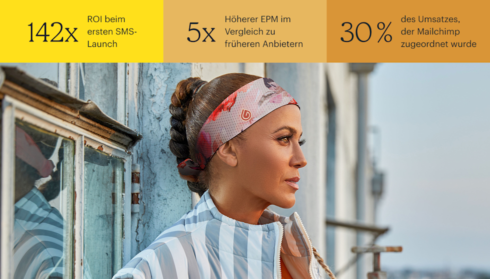 Die Schauspielerin Nicole Ari Parker steht im Freien neben einem verwitterten Gebäude und schaut nachdenklich in die Ferne. Im Hintergrund sind leicht verschwommen die Umrisse der Stadt zu erkennen. Sie trägt ein rosafarbenes gemustertes Gymwrap-Stirnband, und ihre Haare sind zu einer geflochtenen Hochsteckfrisur gestylt. Die wichtigsten Statistiken sind: 142x ROI bei der ersten SMS-Einführung, 5x höherer EPM im Vergleich zu früheren Anbietern und 30 % der Einnahmen, die Mailchimp zugeschrieben werden.
