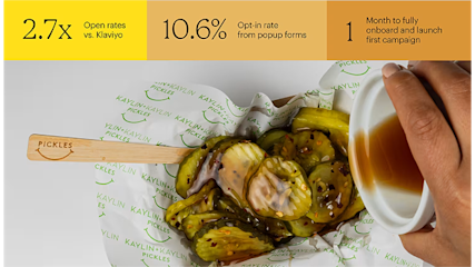 Wooden pickle spoon resting on branded paper next to a jar of pickles with brine, showing restaurant branding and presentation