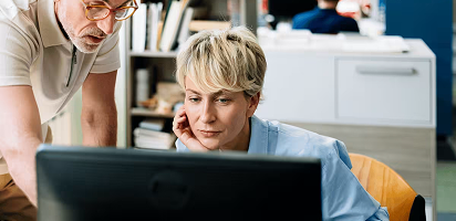 Two people collaborating at a desk while looking at computer screens in a modern office environment