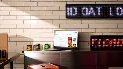 Modern office desk setup with laptop displaying website, LED scrolling display, and white brick wall background