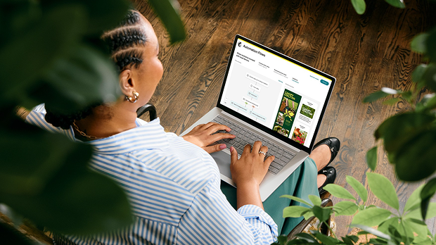 Person in striped shirt working on laptop surrounded by houseplants, viewed from above on wooden floor