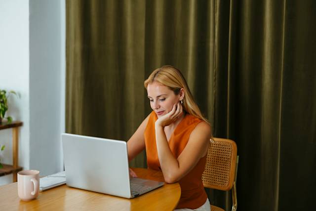 Woman in orange shirt, working on a silver laptop