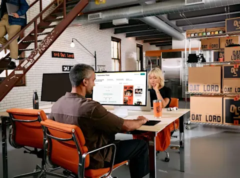 Two people working at desktop computers in the Oat Lord offer