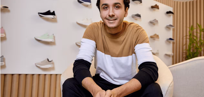 Person in color-block sweater sitting in modern retail space with athletic shoes displayed on wall behind them